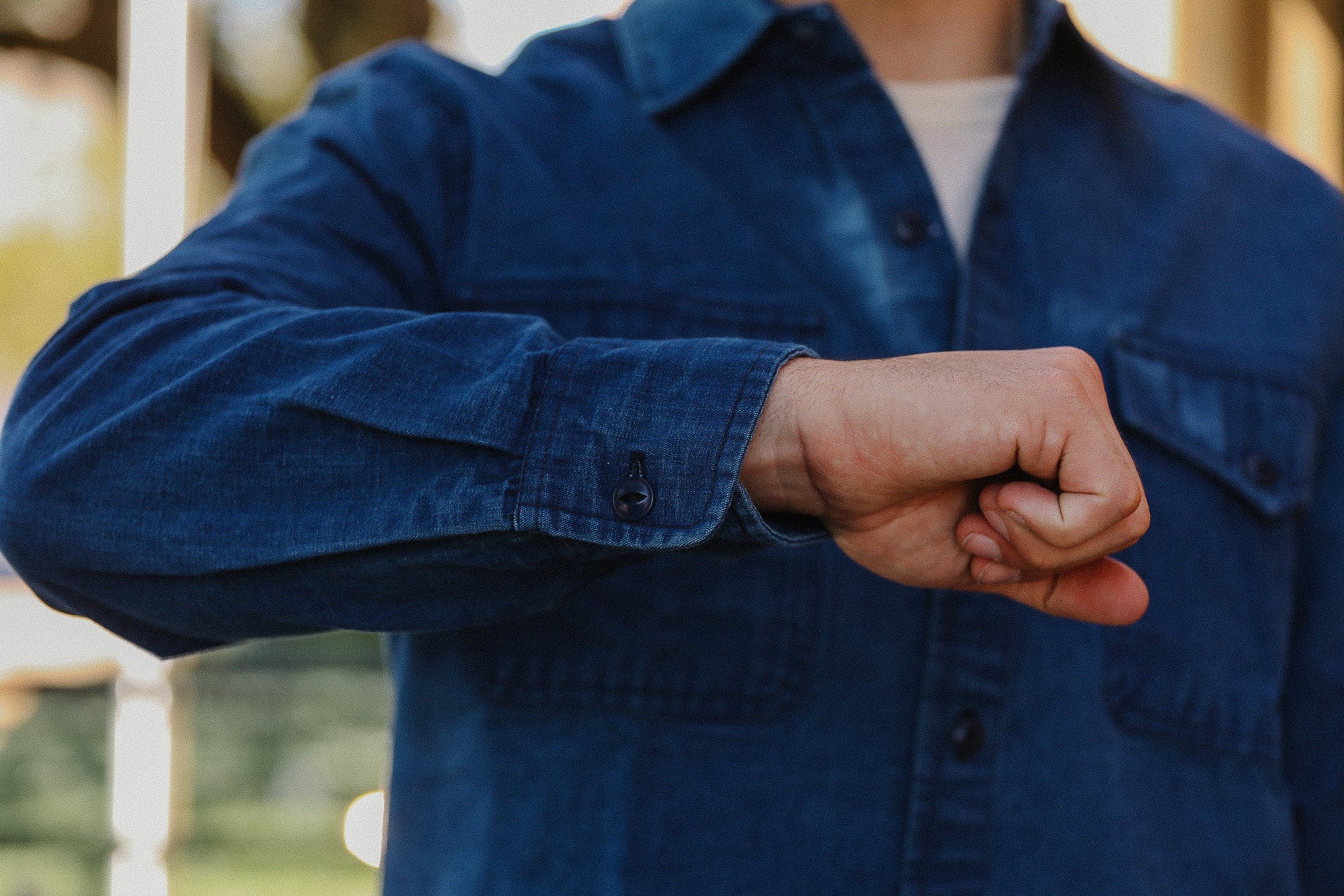 Person wearing blue denim shirt showing clenched fist in casual outdoor setting