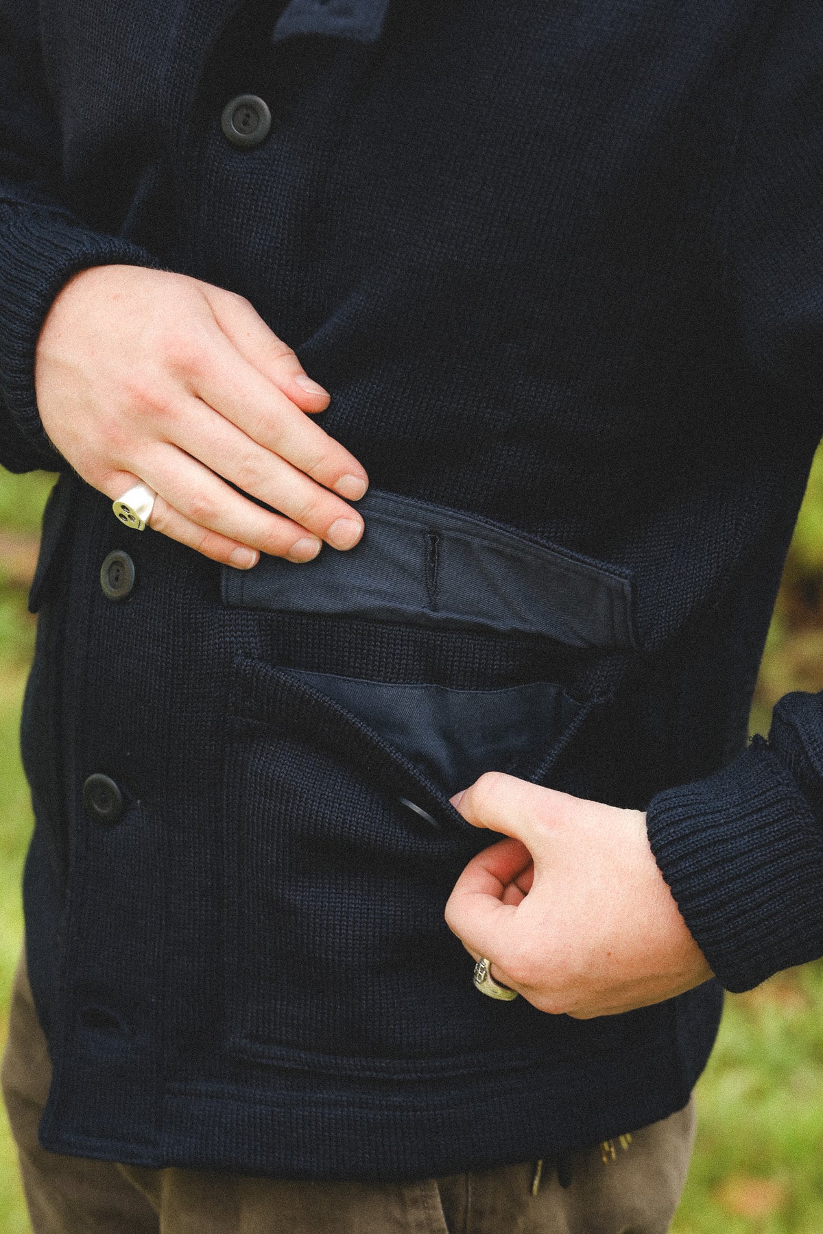 Close-up of a person wearing a dark navy ribbed knit cardigan with front pockets, showing hands opening the pockets.