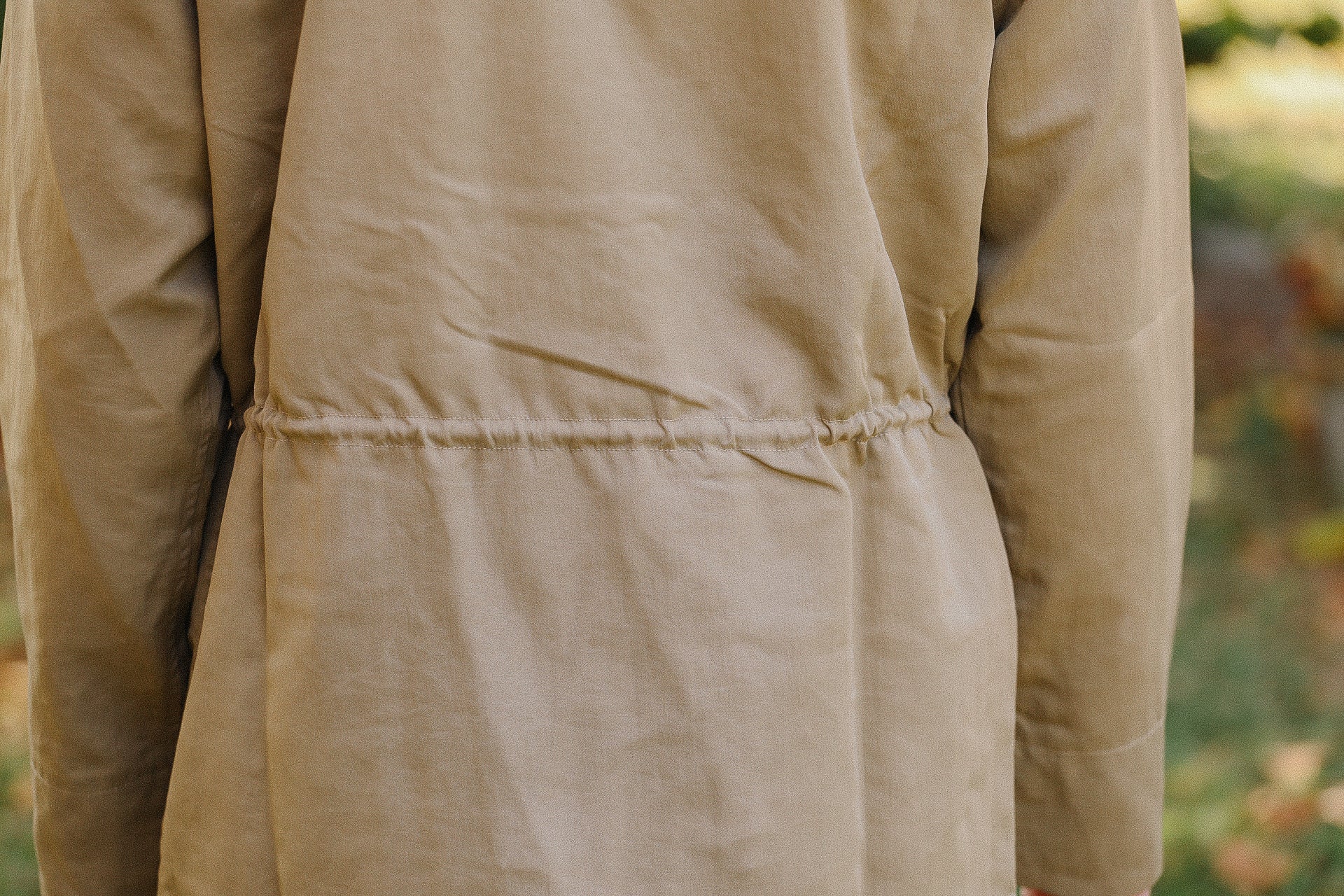 Close-up of beige cotton jacket back with cinched waist stitching in outdoor setting