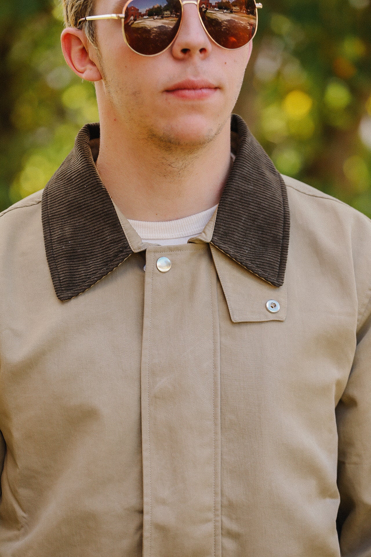 Close-up of a man wearing tan work jacket with dark corduroy collar and reflective aviator sunglasses