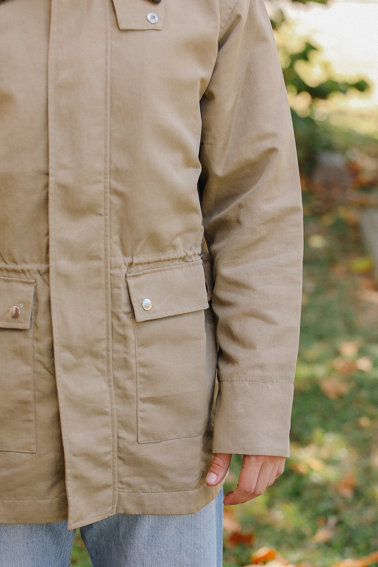 Close-up of a person wearing a tan work jacket with snap button pockets outdoors in a natural setting