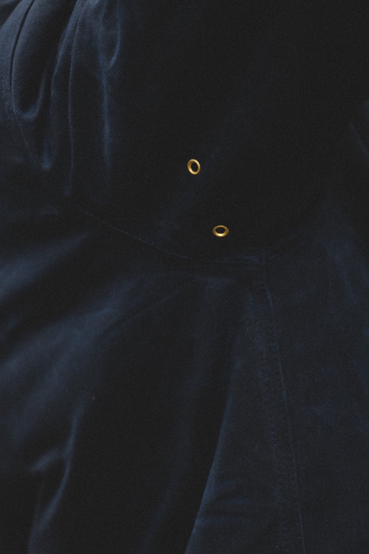 Close-up of a dark navy blue velvet or velour fabric surface with two small gold-tone eyelet details near the center.