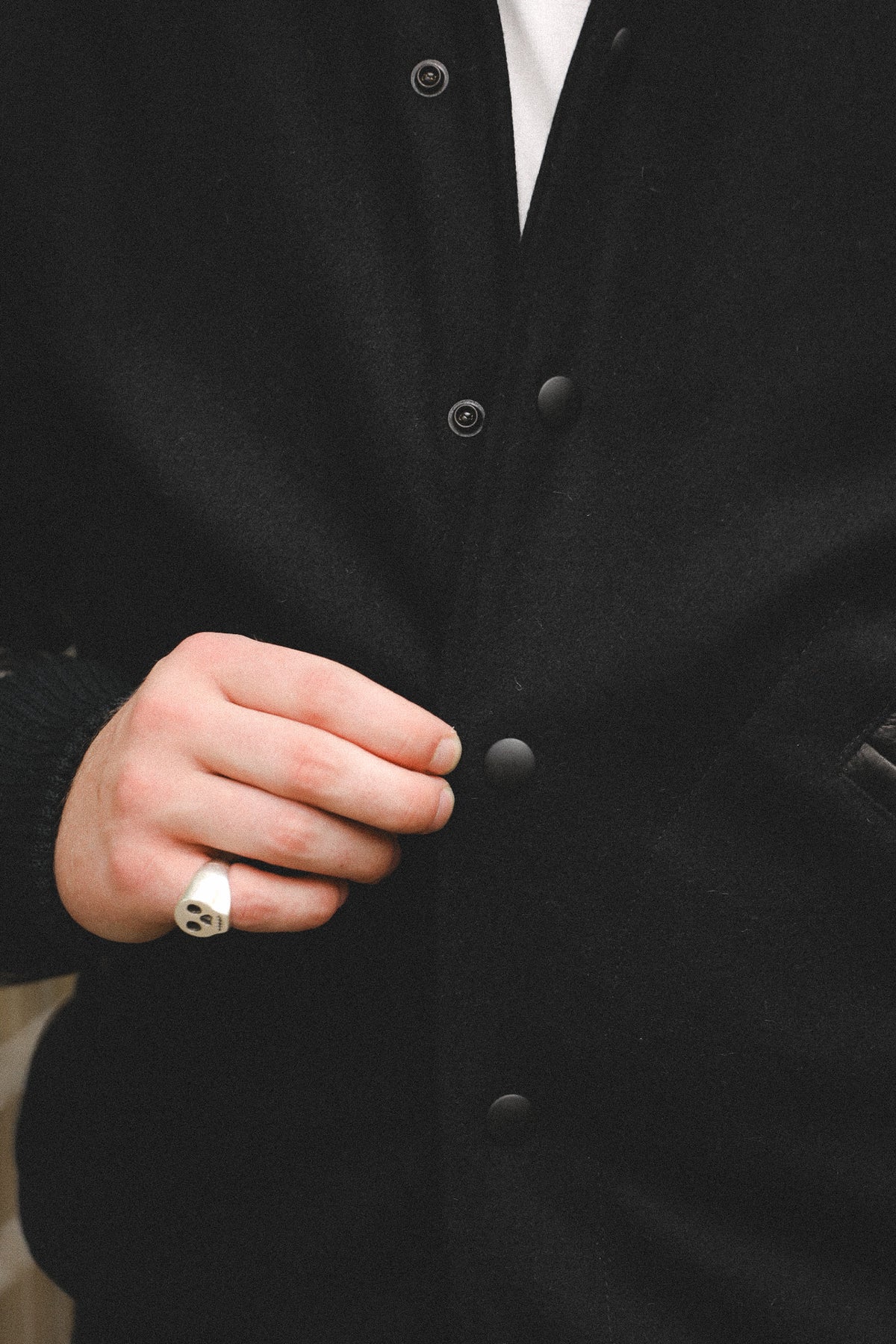 Close-up of a person wearing a black knit button-front cardigan over a white shirt, with one hand adjusting the front and wearing a silver ring.