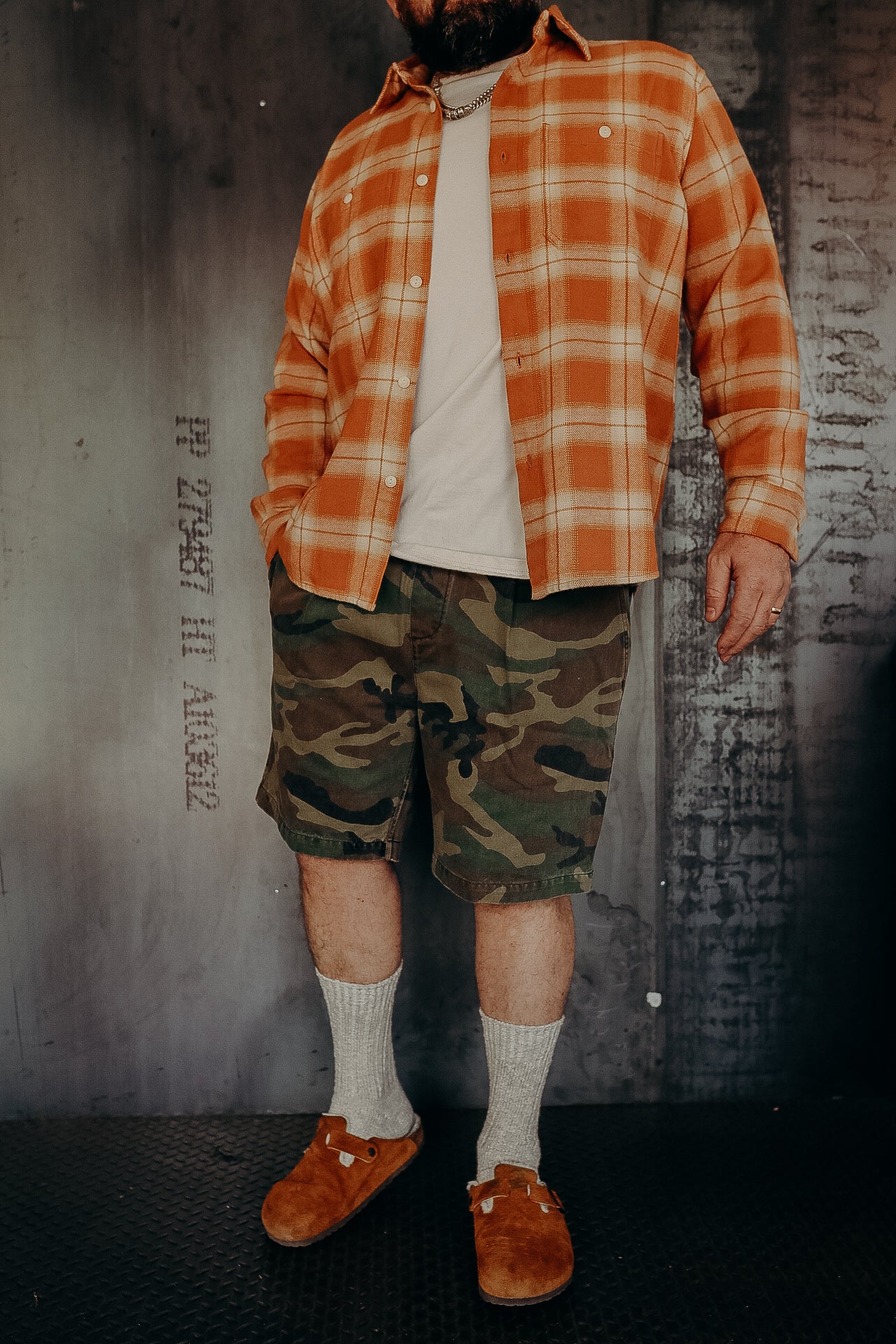 Man wearing orange plaid shirt, white t-shirt, camouflage shorts, gray socks, and brown slip-on shoes