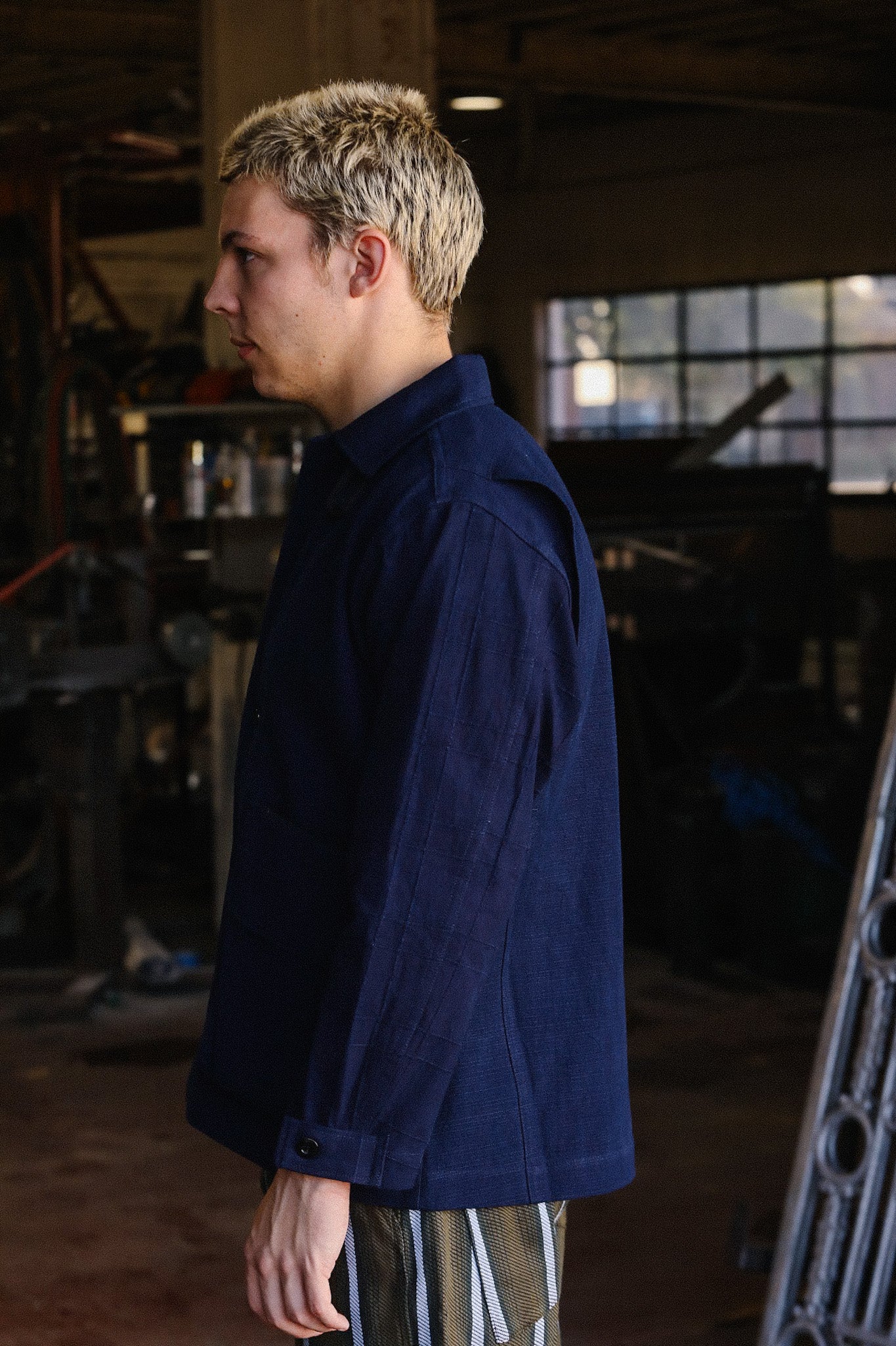 Side profile of a man with blonde hair wearing a navy blue shirt in a rustic industrial workshop