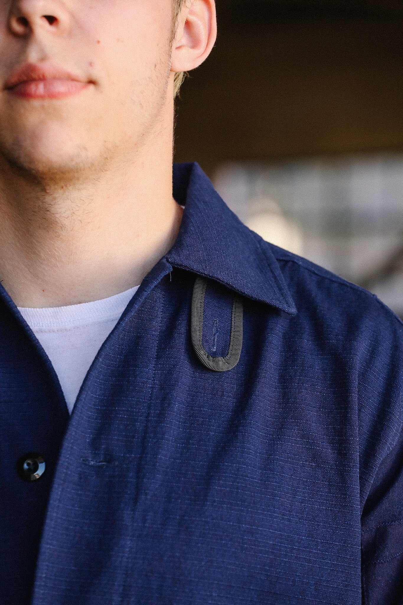 Close-up of a man wearing a dark blue collared iron work shirt with a unique loop detail near the collar