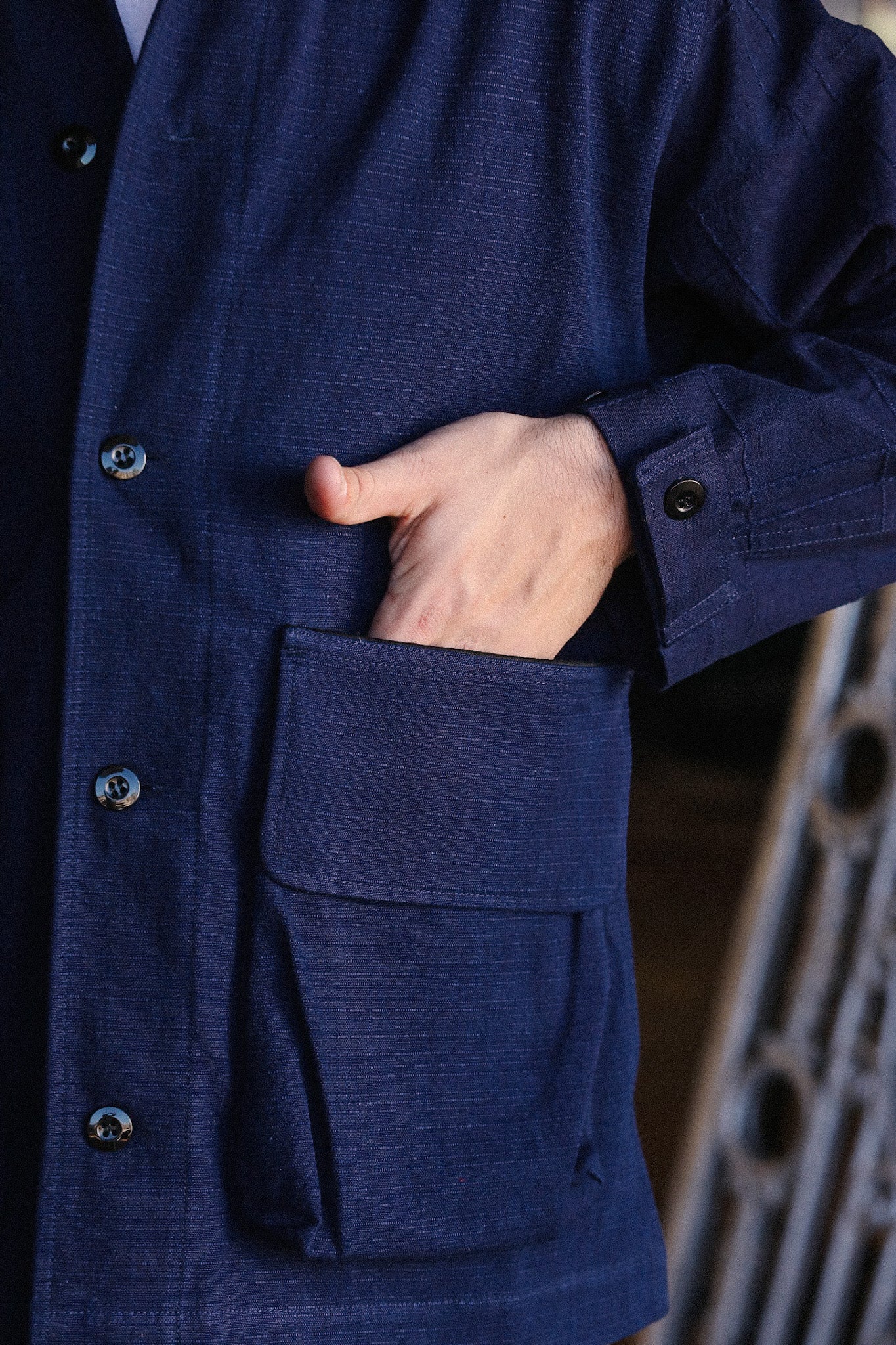 Close-up of hand inside large front pocket of navy blue button-up work jacket