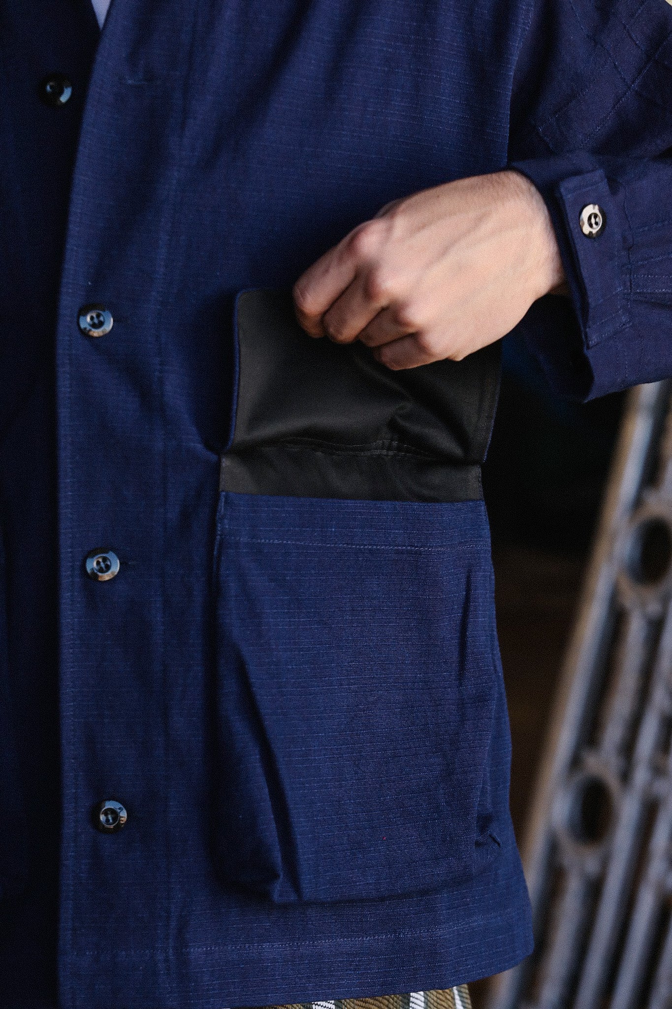 Close-up of hand putting black wallet into large front pocket of navy blue button-up shirt