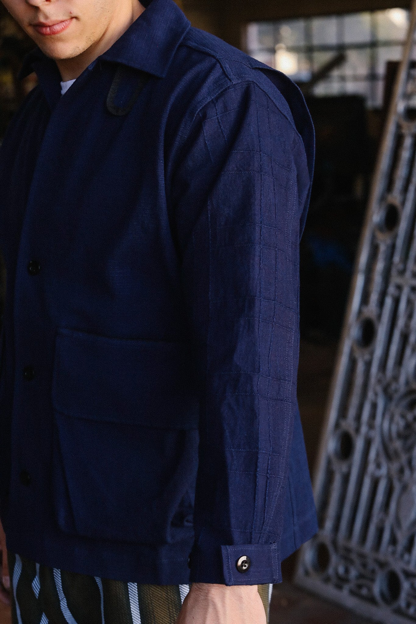 Close-up of a man wearing a navy blue jacket with large pockets and button cuffs, standing indoors