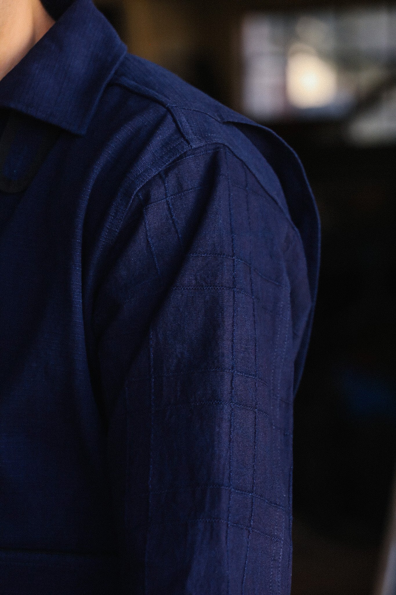 Close-up of navy blue textured shirt sleeve with stitched detailing in a dimly lit setting