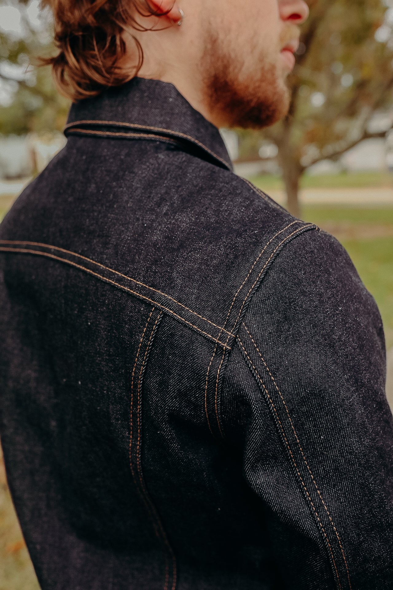 Close-up of man wearing dark denim jacket with contrast stitching outdoors at Iron Shop Provisions