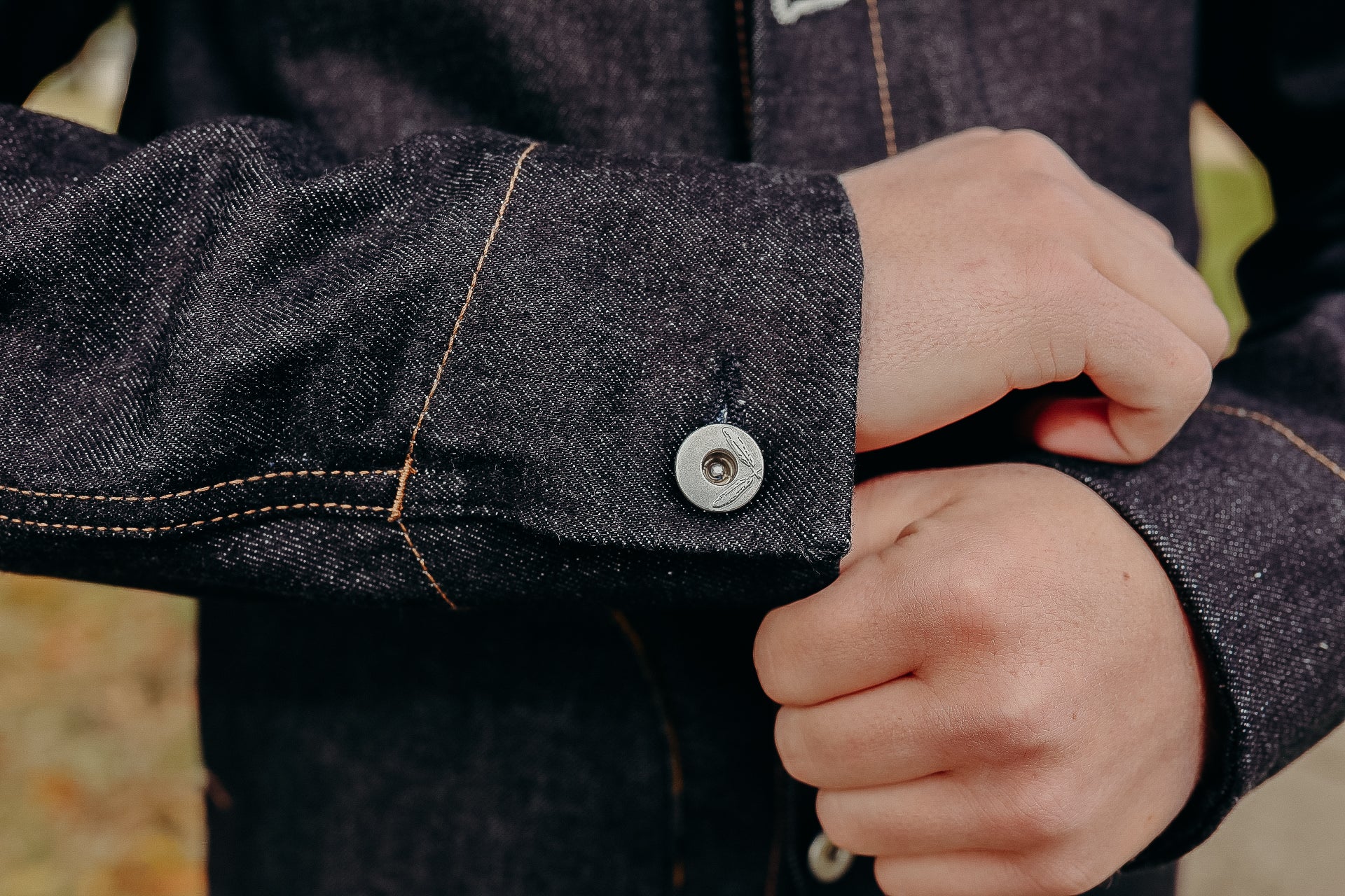 Close-up of hands adjusting sleeve cuff of dark denim jacket with metal button and contrast stitching