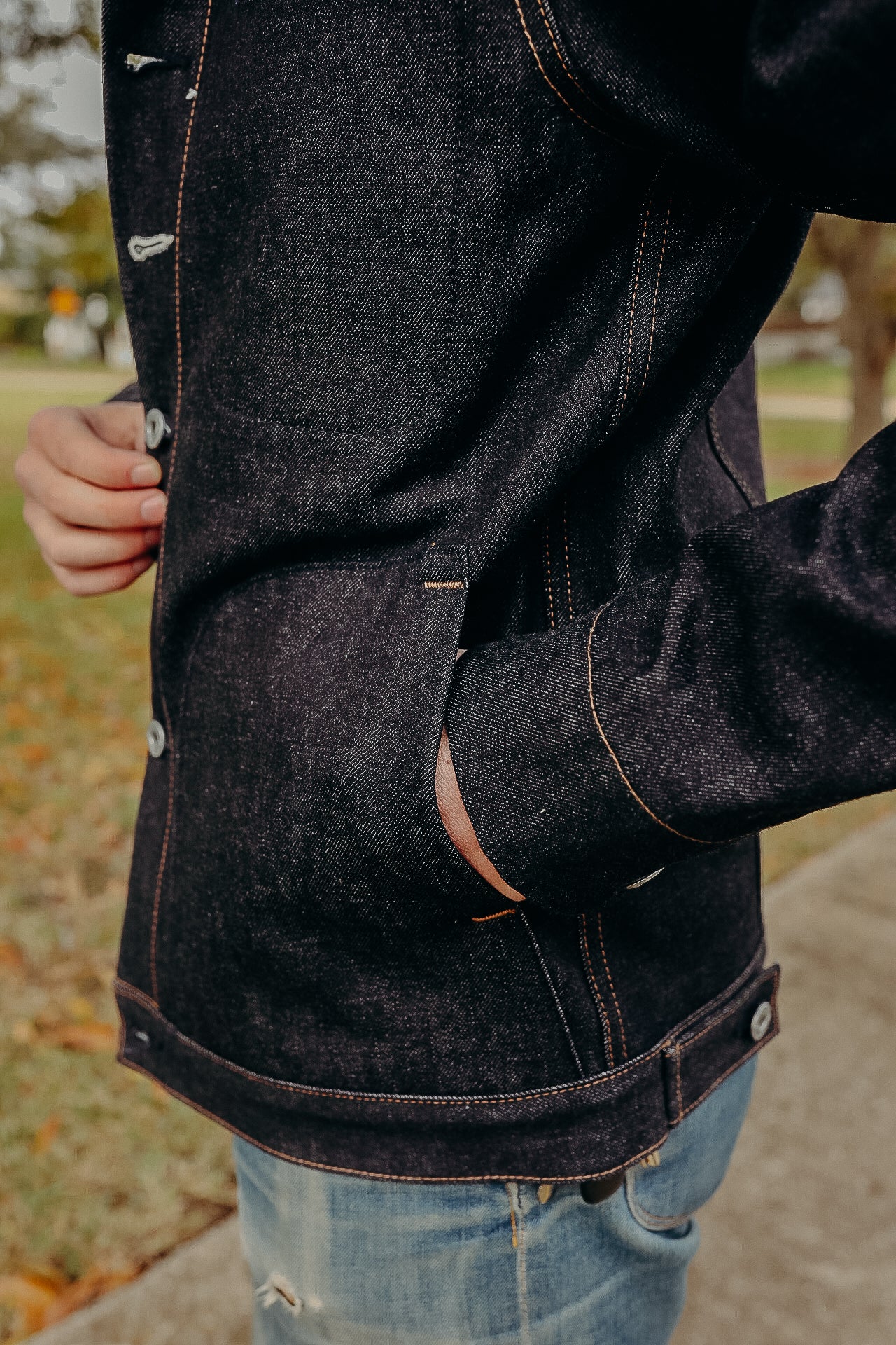 Close-up of person wearing dark raw denim jacket with orange stitching and blue jeans outdoors