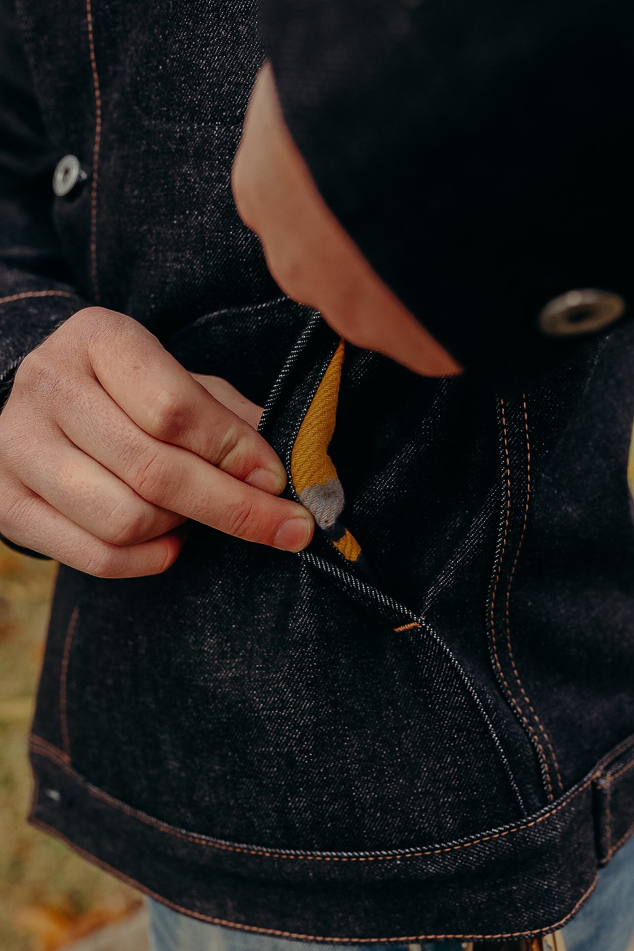 Close-up of person pulling coin from pocket of dark denim jacket with orange stitching