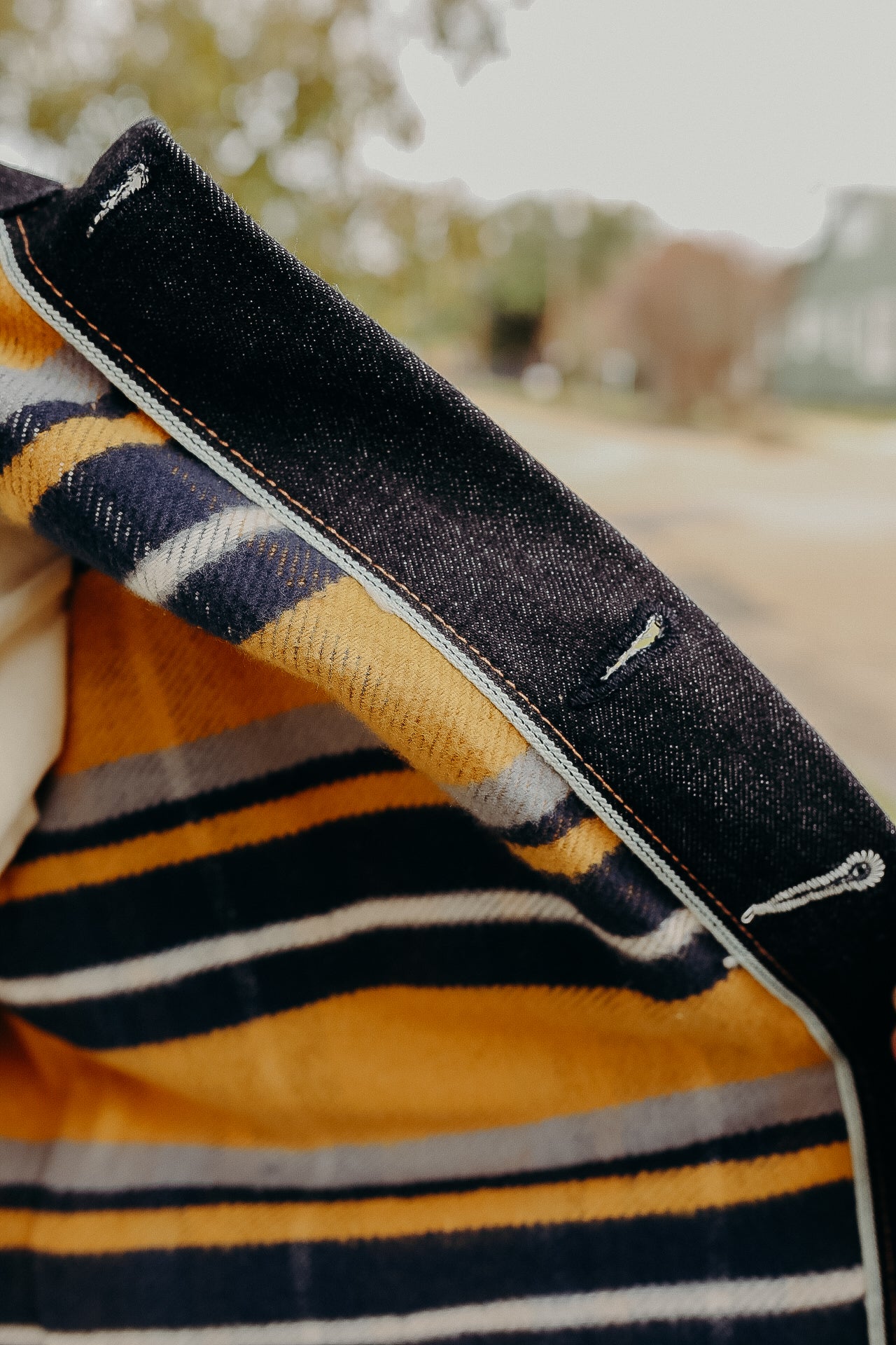 Close-up of denim jacket collar with striped yellow, navy, and gray wool lining outdoors