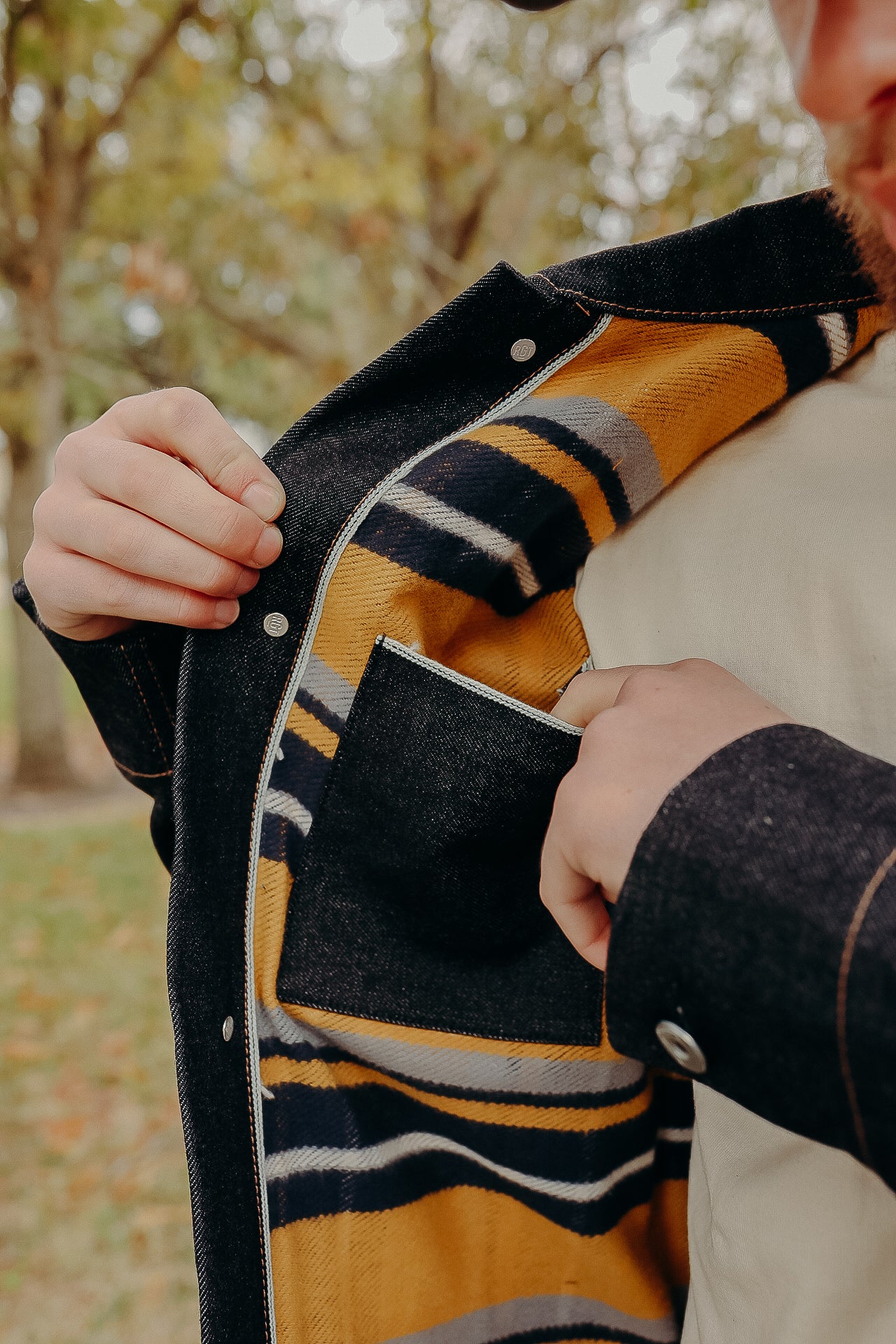 Close-up of a person showing the striped yellow and black plaid interior lining of a dark denim jacket outdoors