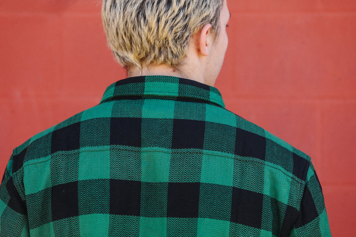 Back view of person wearing green and black checkered flannel shirt against red brick wall