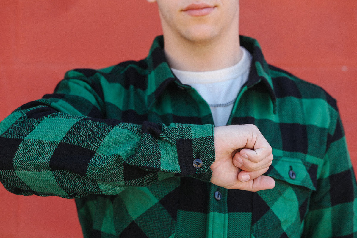 Man in green and black plaid flannel shirt against red wall, showing wrist and casual style