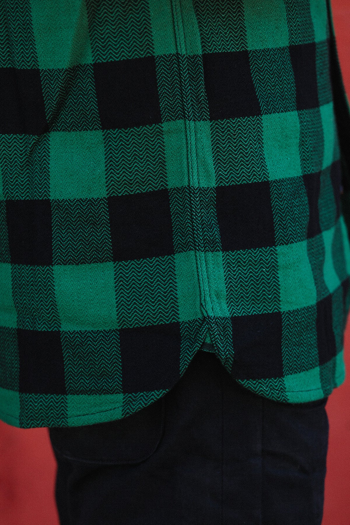 Close-up of green and black checkered flannel shirt hem over dark pants on red background