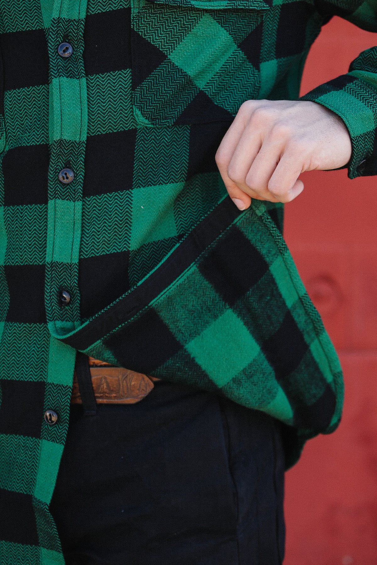 Close-up of person wearing green and black checked flannel shirt from Iron Shop Provisions, showing shirt hem and black pants