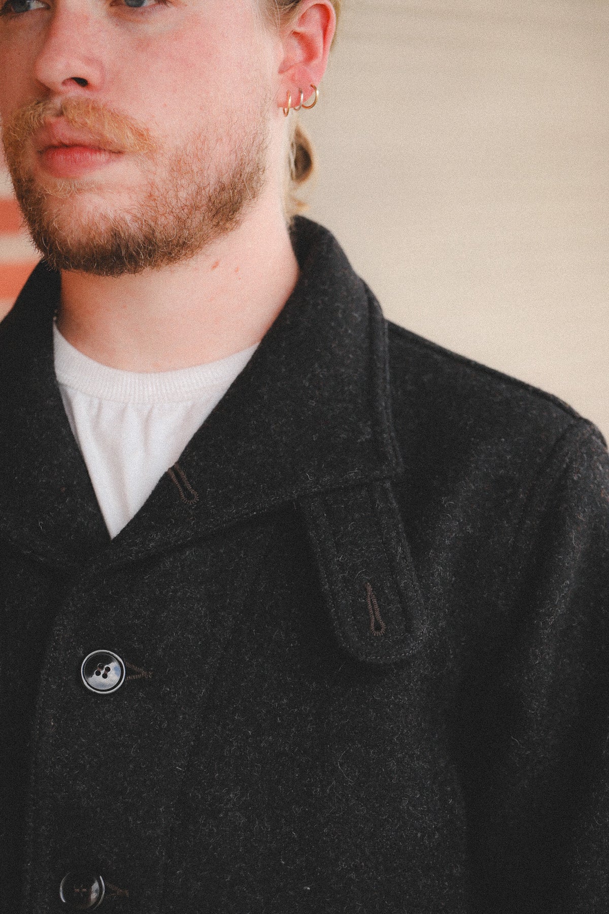 A person  wearing a dark charcoal gray wool-blend coat, standing in front of a red brick wall and a metal roll-up door.