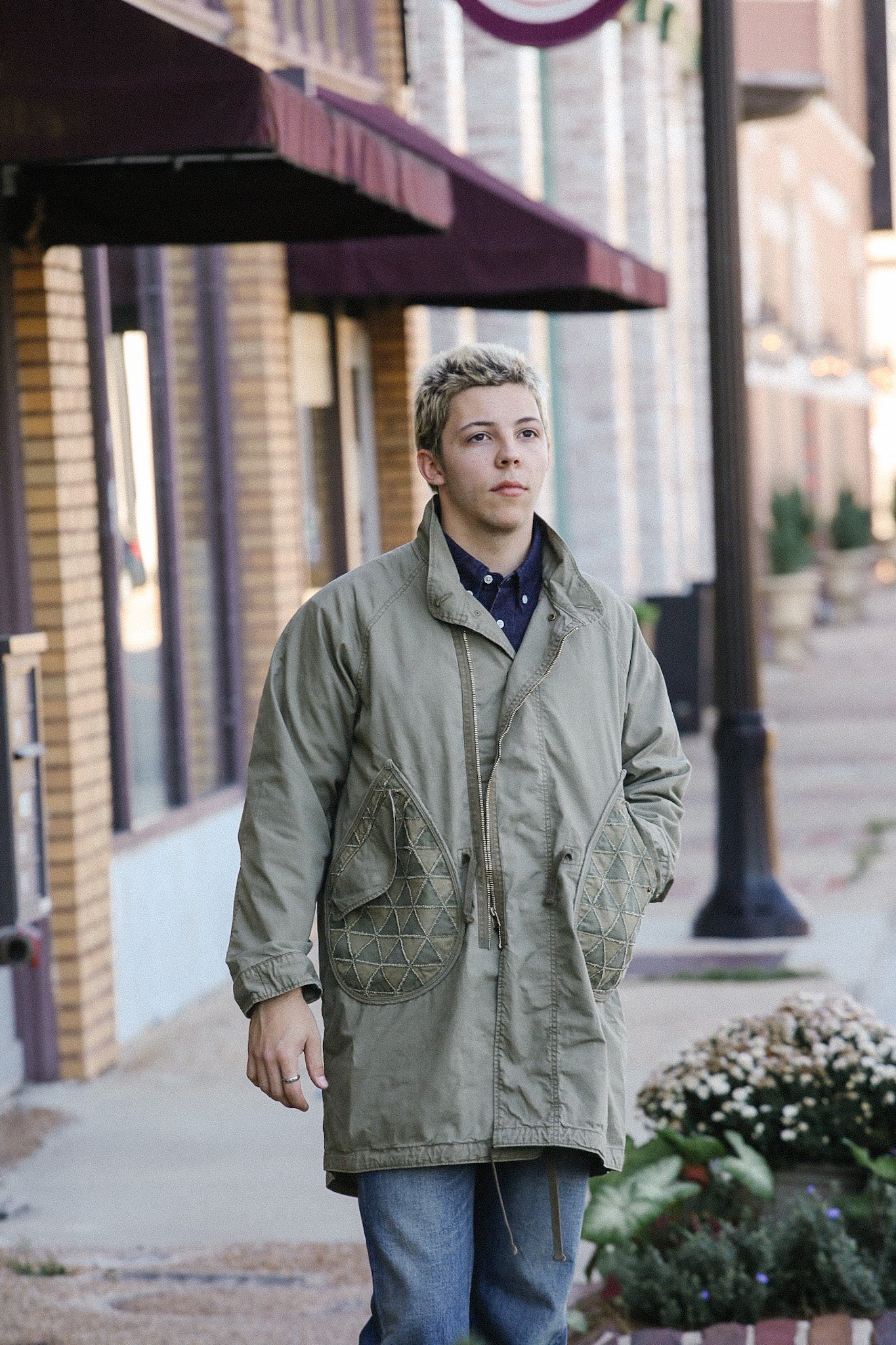 Young man wearing olive green vintage military jacket with quilted pockets walking on downtown sidewalk