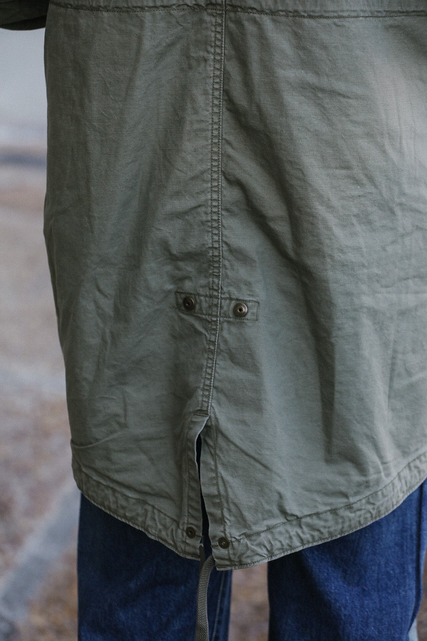 Close-up of olive green utility jacket hem with metal snaps and blue jeans by Iron Shop Provisions