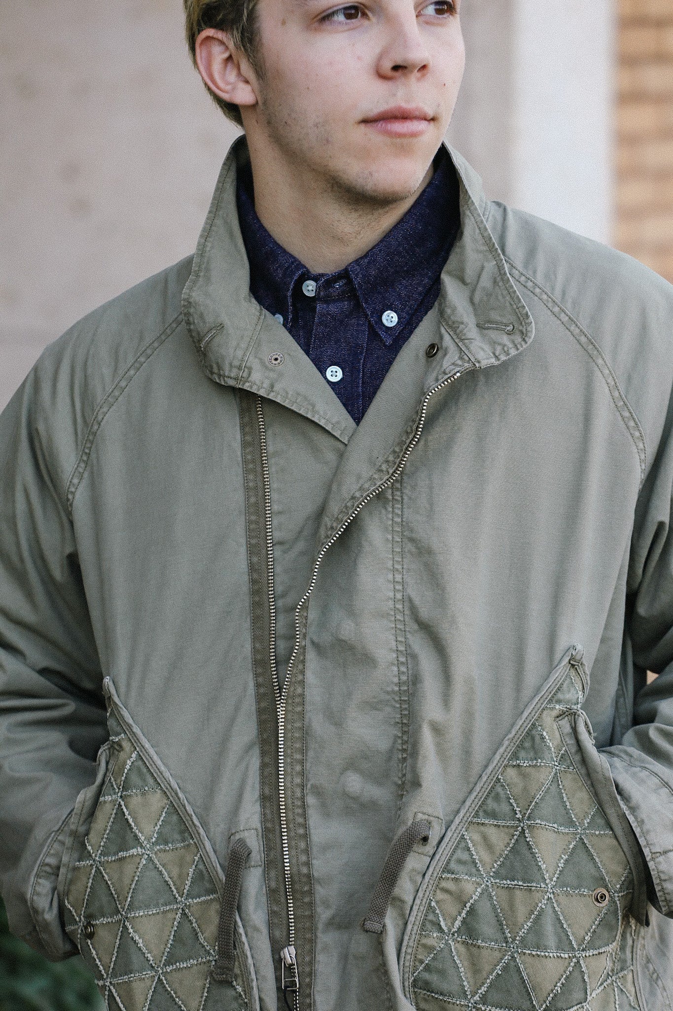 Close-up of man wearing an olive green utility jacket with quilted geometric pockets and a navy button-up shirt
