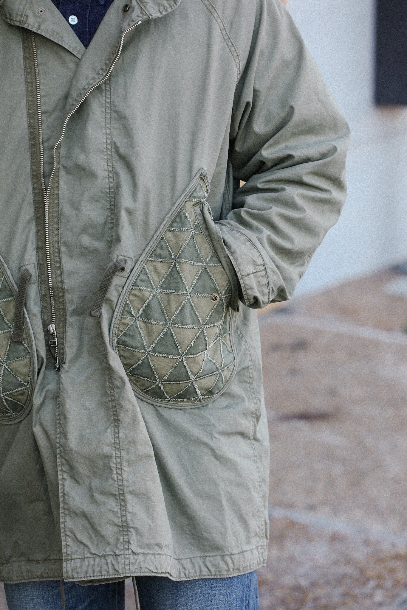 Close-up of person wearing olive green jacket with quilted pockets and zipper, styled with blue jeans