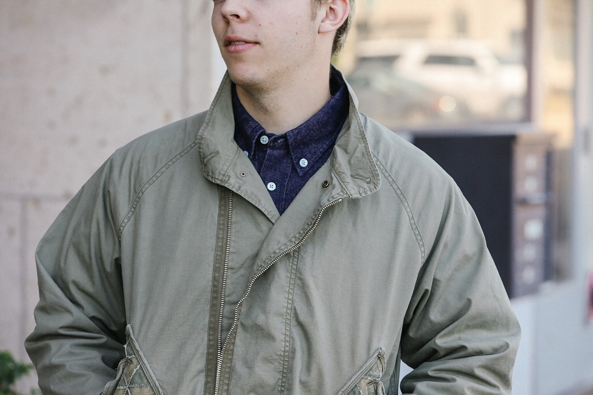 Man wearing vintage green military-style jacket over navy button-up shirt outdoors