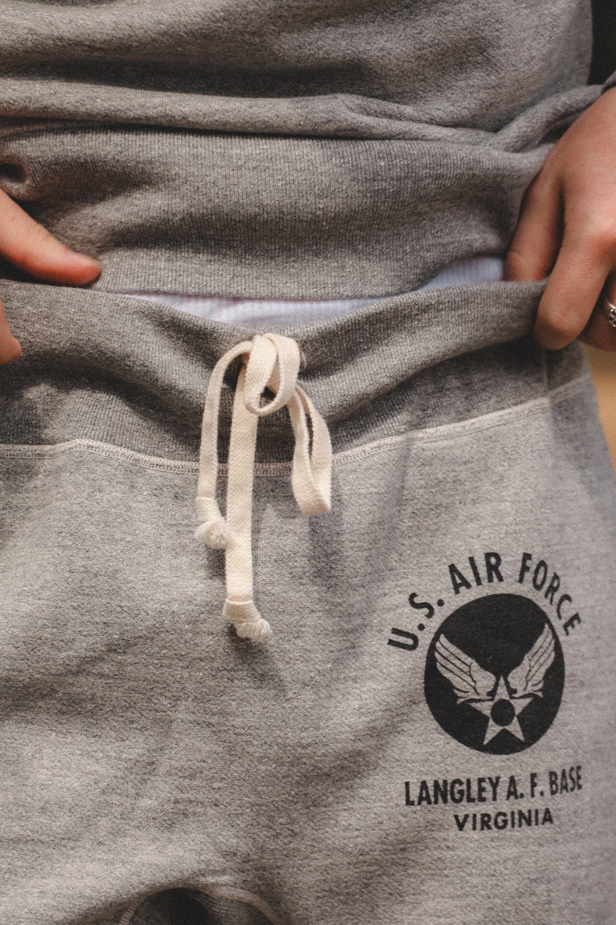 Close-up of a person wearing heather gray sweatpants with a white drawstring and a black U.S.