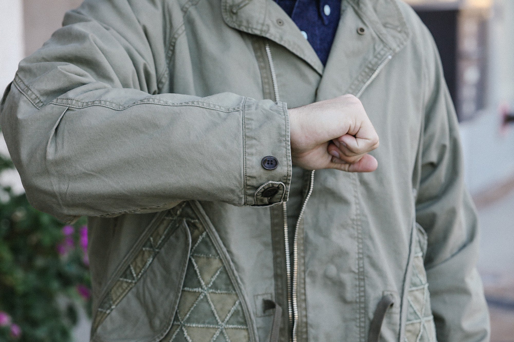 Close-up of a person wearing a green military-style jacket with zipper and button details, outdoor setting