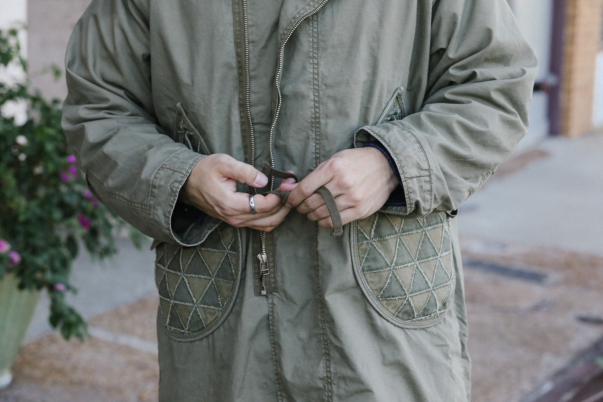 Close-up of hands tying strap on olive green utility jacket with quilted pockets outdoors