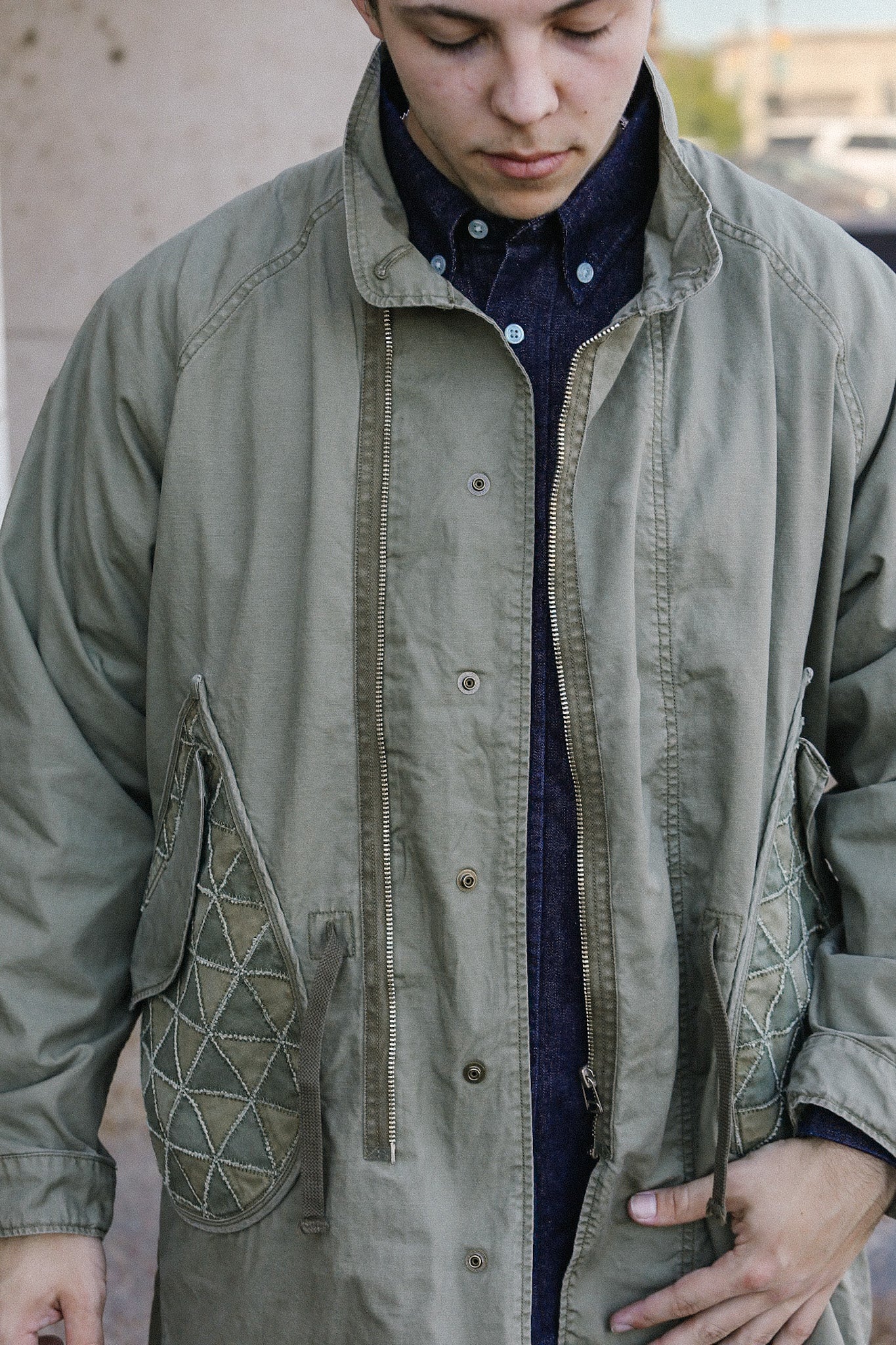 Close-up of a man wearing a green vintage military-style jacket with quilted pockets over a dark button-up shirt