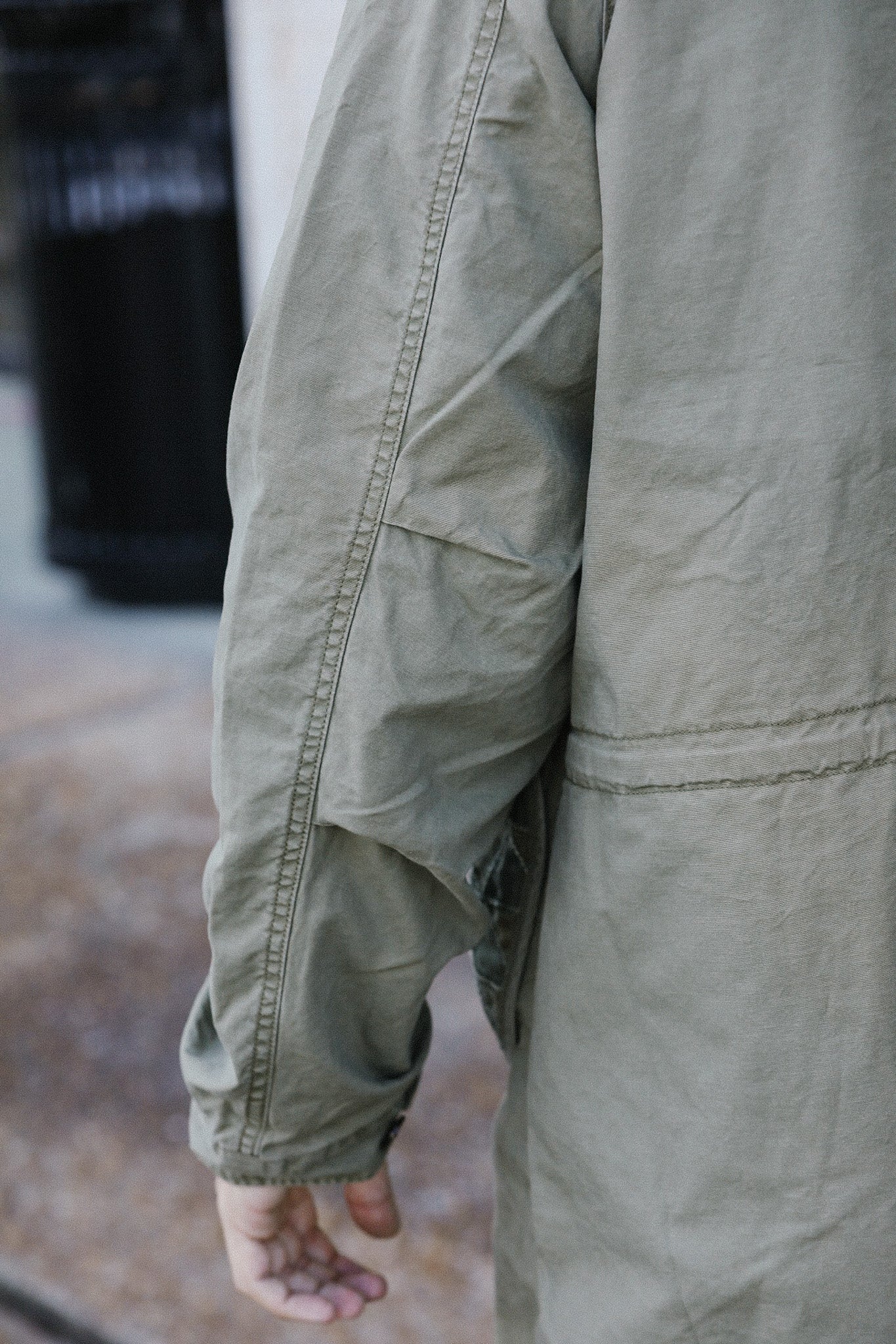 Close-up of a person wearing an olive green work jacket with visible stitching, outdoors
