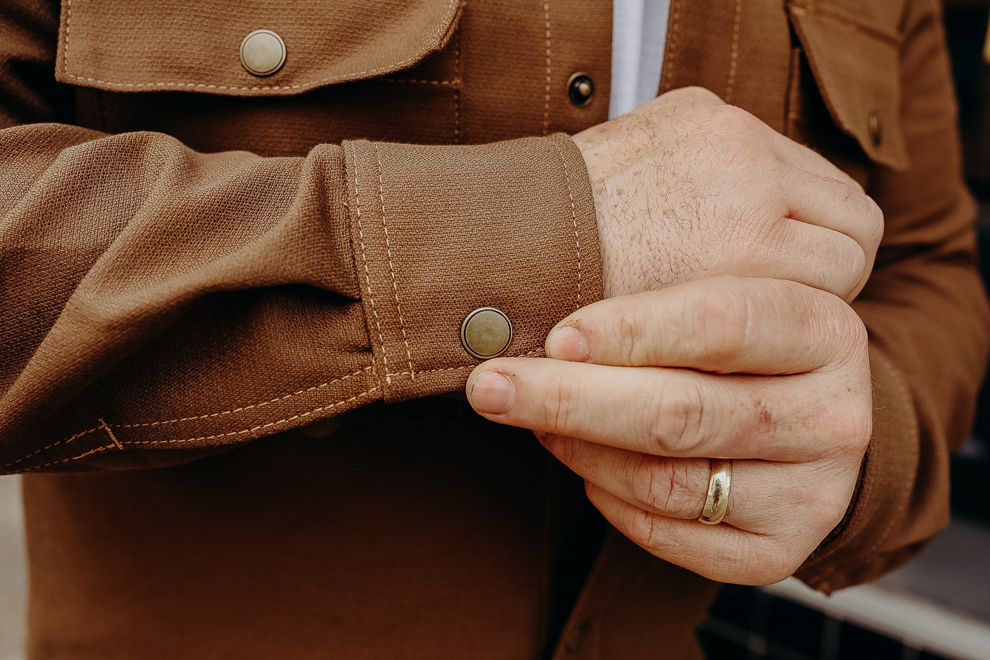 Close-up of hands fastening a bronze snap button on a rugged brown work jacket cuff