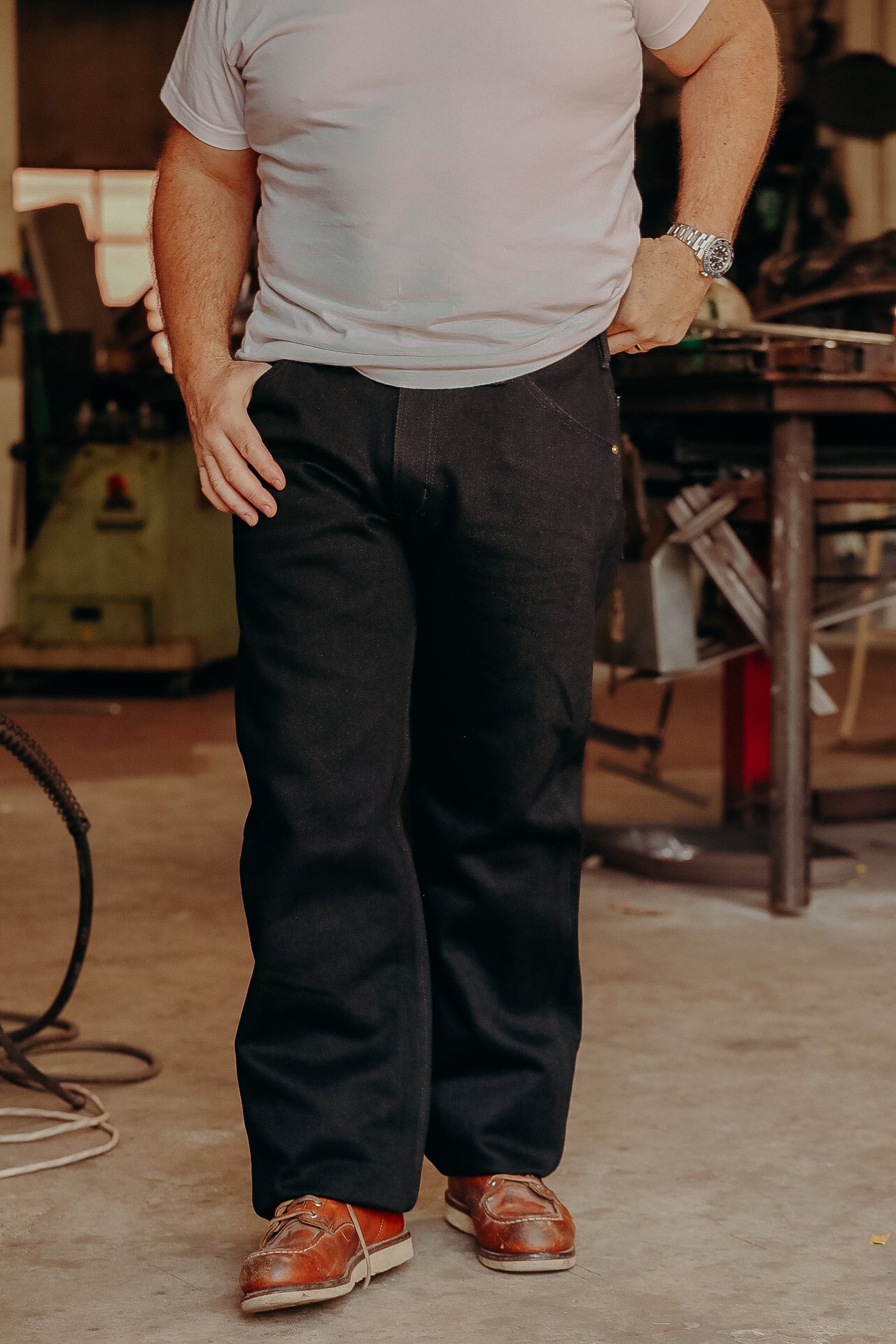 Man wearing black work pants and brown leather boots inside an industrial workshop