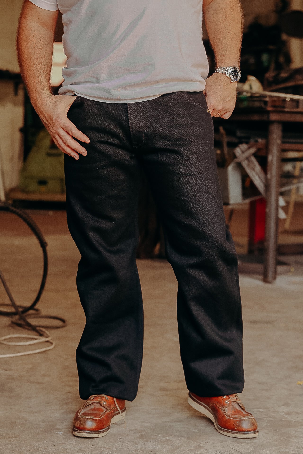 Man wearing black work pants, brown leather boots, and a white t-shirt in workshop setting