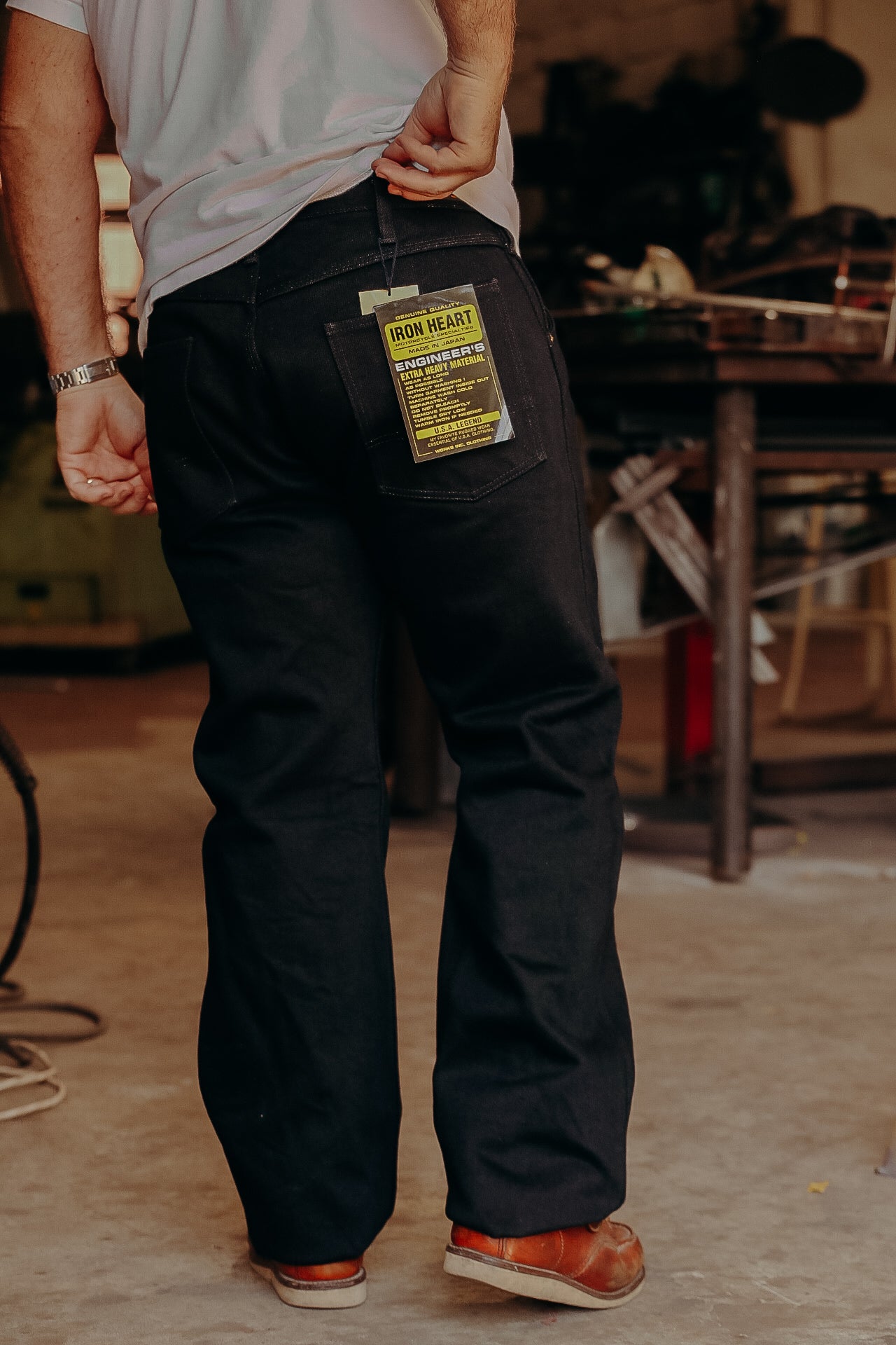 Man wearing black Iron Heart heavy material engineer jeans standing in workshop with tag visible
