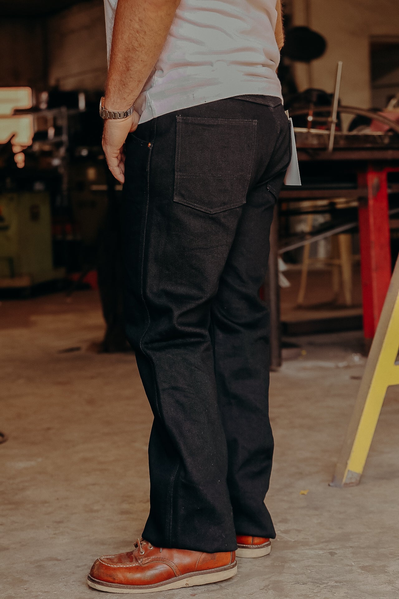 Man wearing black denim work jeans and brown leather boots in a workshop setting