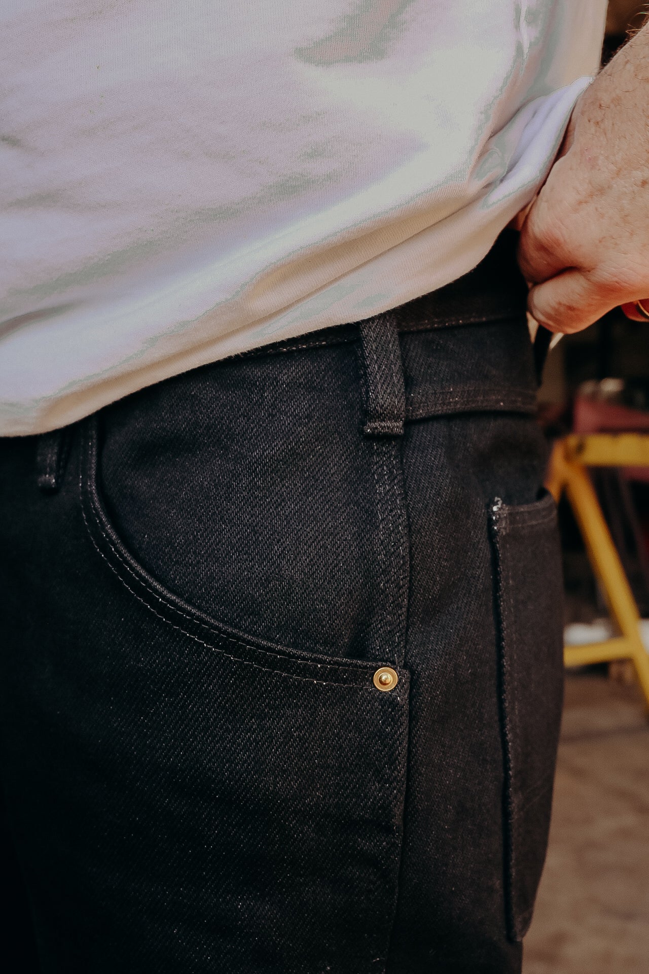 Close-up of black denim jeans pocket with brass rivet and white t-shirt tucked in