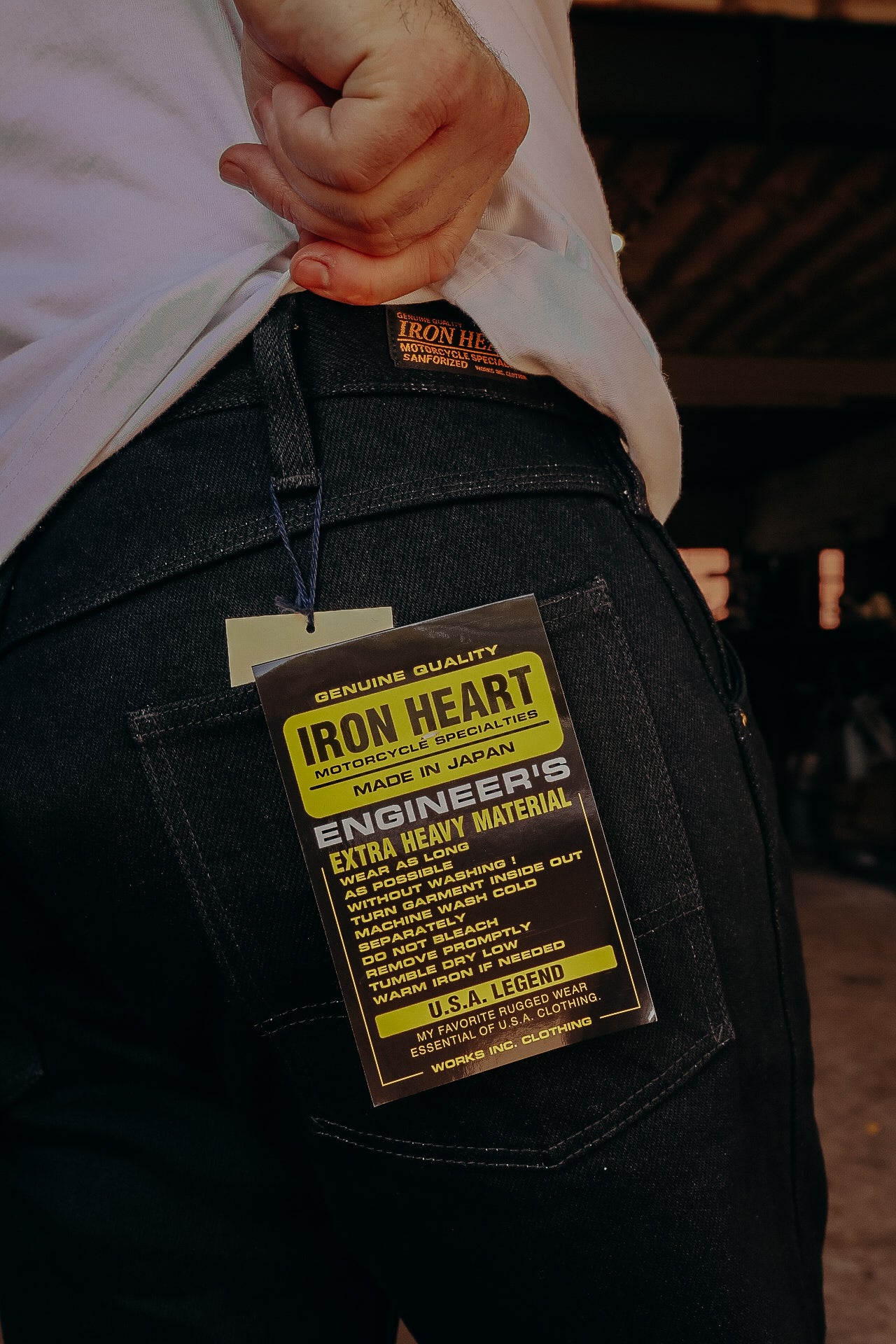 Close-up of black Iron Heart jeans with branded tag showing extra heavy material and care instructions
