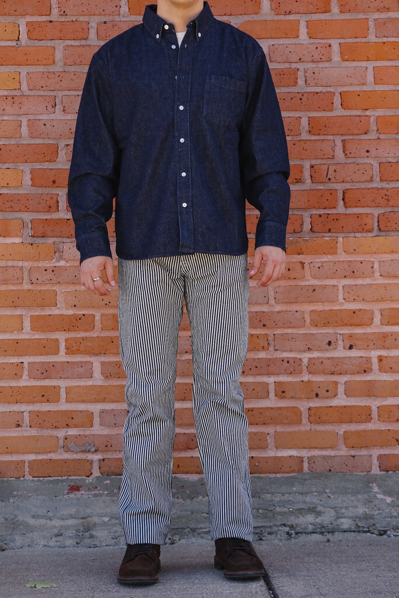 Man wearing dark navy button-up shirt and striped pants standing against a brick wall