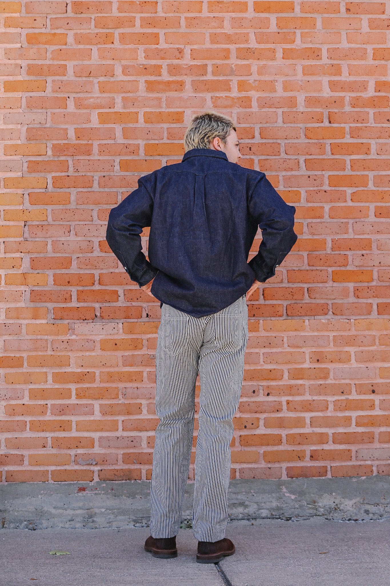 Man wearing navy blue shirt and striped pants standing with back to brick wall