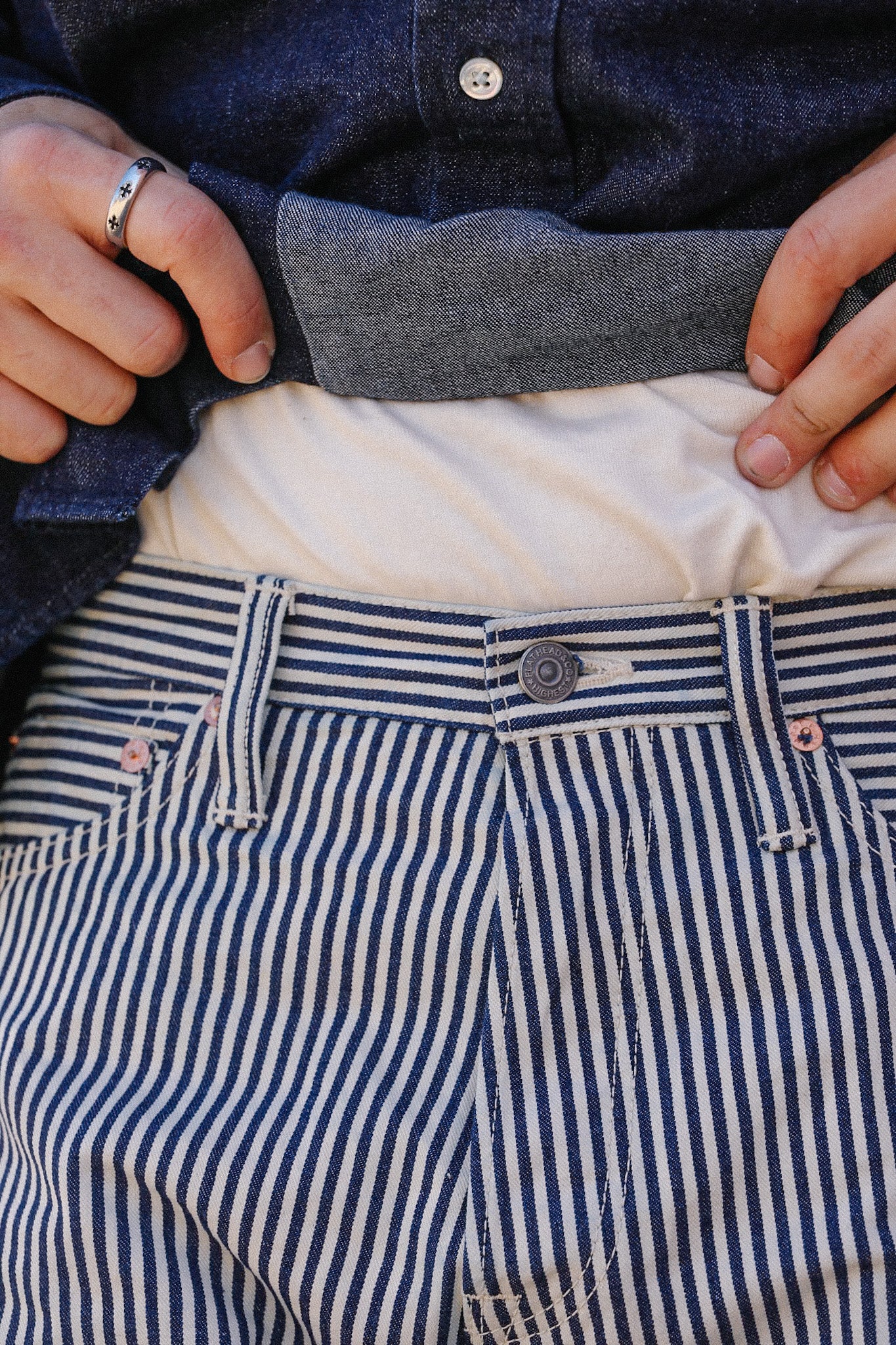 Close-up of striped blue and white denim pants with hands adjusting a dark denim shirt at Iron Shop Provisions