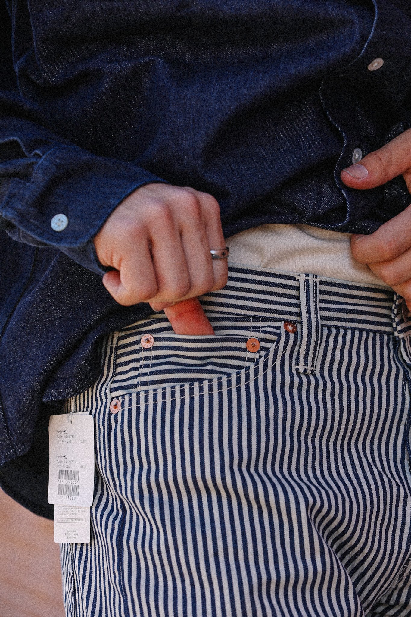 Close-up of person wearing striped denim pants with price tag and dark blue shirt at Iron Shop Provisions