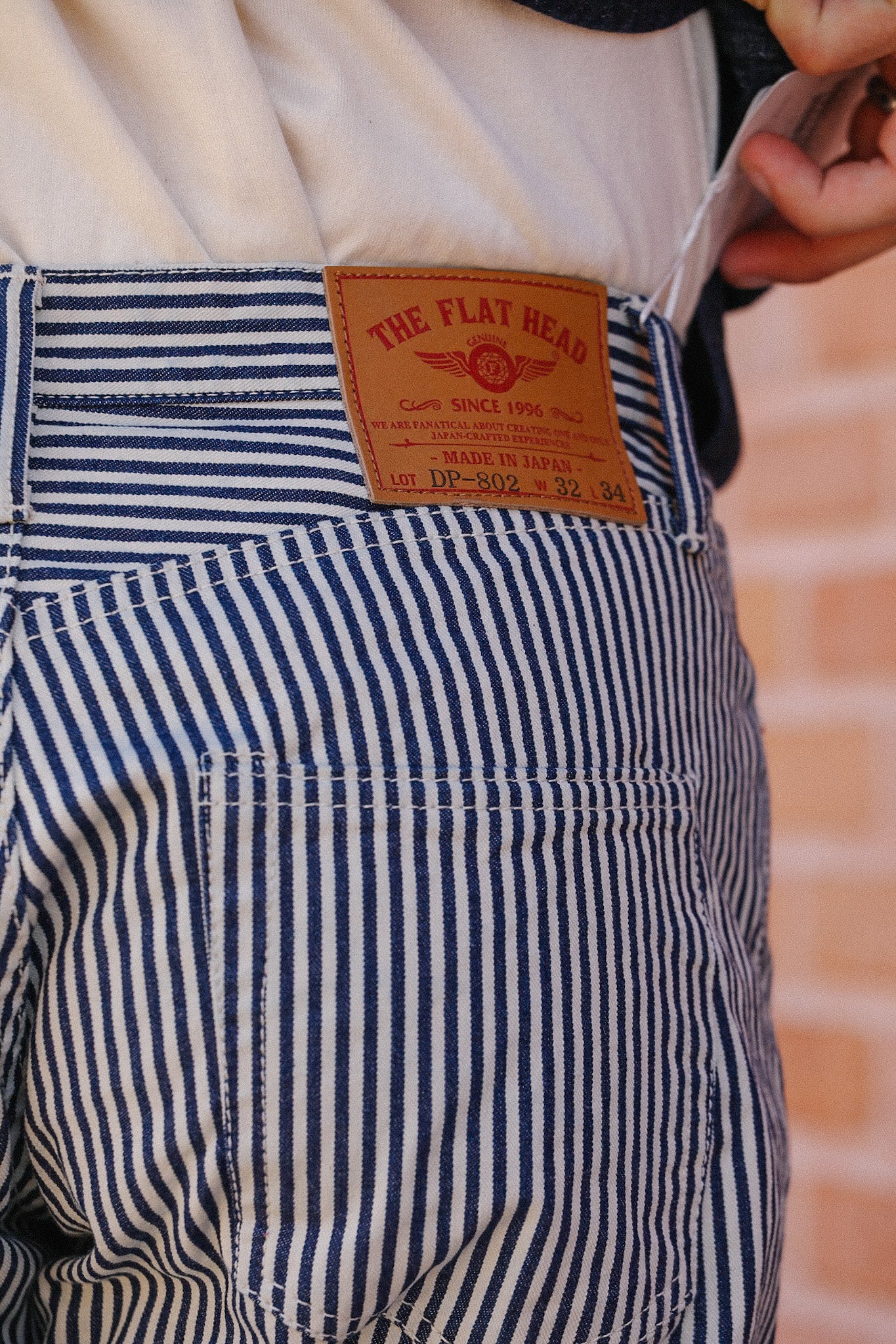 Close-up of blue and white striped pants with leather label reading The Flat Head, made in Japan