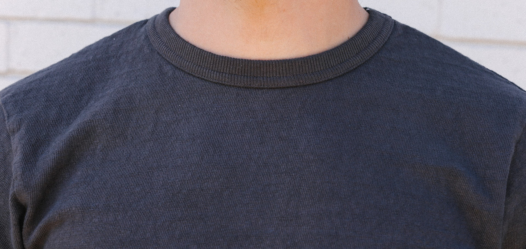Close-up of a person wearing a dark gray ribbed crew neck shirt against a light background