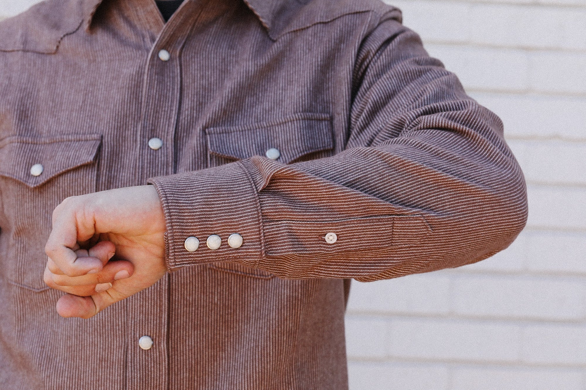 Close-up of a man wearing a brown striped work shirt with snap buttons and chest pockets