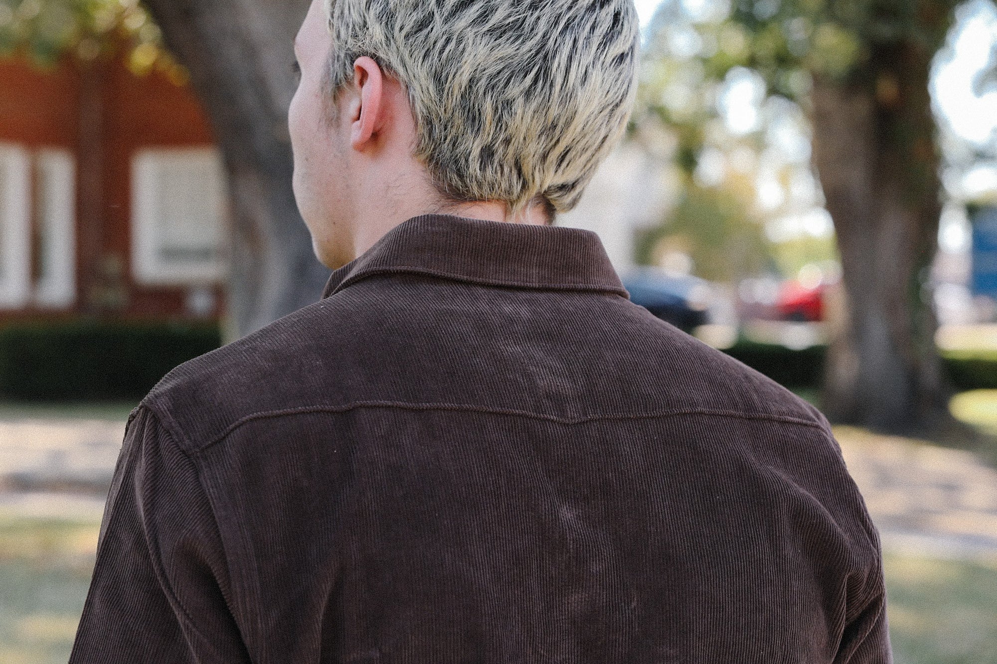 Back view of person with short blonde hair wearing a brown corduroy jacket outdoors
